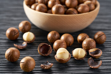 macadamia spill out of a wooden bowl on a black table, selective focus.