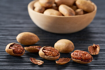 Pecan spill out of a wooden bowl on a black table, selective focus.