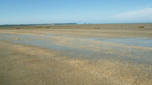 A walk on the vast flat coastline of Saint Benoit Des Ondes, Brittany, France, during low tide. Small shells on the ground with sand. The atlantic ocean is visible in the distance.
