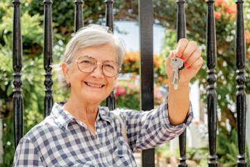 Blurred smiling senior woman at gate holding keys to new home, real estate, buying, renting...