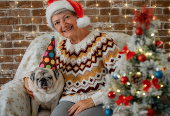 Portrait of senior woman at christmas time sitting together her pug dog on the sofa near the...