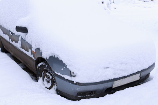 A parked passenger car was covered with snow in an open parking lot due to heavy snowfall