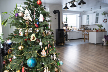 Christmas tree in the white interior of a house with large windows. Glowing fairy lights garlands interior decoration of the studio room. Potted plants in the home