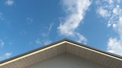 Gable corner of the roof of the central house used metal cheese roof. Under blue sky and white clouds.