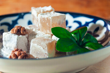 Cubes of Turkish delight on a national Uzbek plate with walnuts. Close-up shooting.
