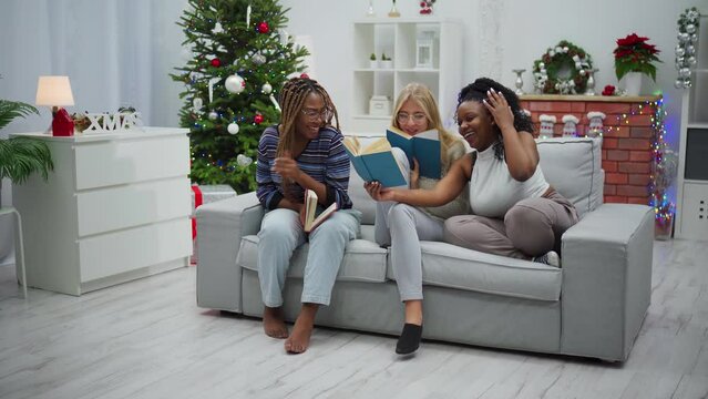 The girls sit on the sofa and read funny stories in a book.