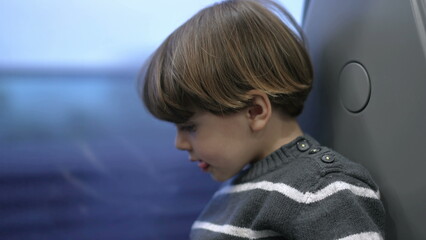 Fototapeta premium One small boy traveling by train staring at window with landscape passing by. Child travels on high speed train