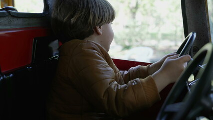 One happy small boy driving toy car interior at amusement park carousel. Child holding steering...