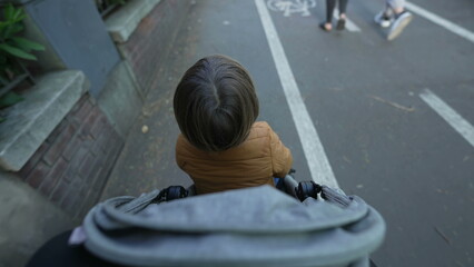 Child sitting in stroller. Parent POV walking in city street with toddler son. Mother pushing baby carriage point of view