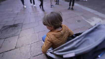 One child sitting in a stroller strolling in European street. 2 year old small boy seated. mother perspective
