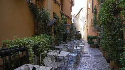 Old European street with tables and chairs on cobblestone urban Italian alley with nobody