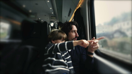 Child seated on father lap pointing finger at landscape while traveling by train. Parent and child staring at window