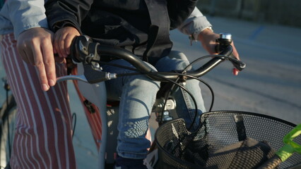 Closeup mother hands holding bicycle handle with child seated in front in baby bike chair riding alternative transportation