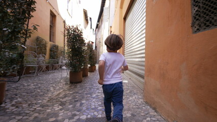 Obraz na płótnie Canvas Back of child running in old european street. One little boy runs in Italian alley