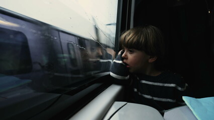 One sad little boy looking out train window in motion. Melancholic child seated by window staring at landscape passing by with depressed expression