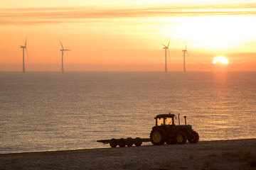 Misty morning sunrise. Beach tractor with offshore wind farm turbines. Eco landscape image for...