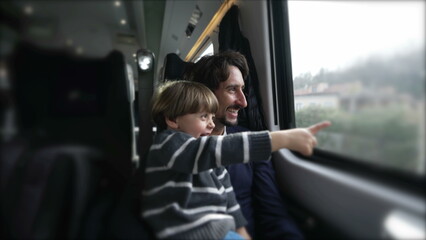 Happy father and son traveling together by train during vacation holidays. Little boy pointing with hand at landscape passing by inside transportation in motion © Marco