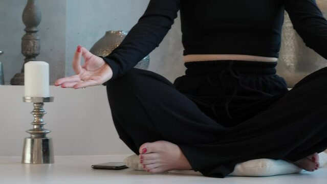 Unrecognizable woman sits cross-legged on karemat, practices meditation. Inner harmony and balance. Lady in black clothes in yoga on karemat, practices meditation, self-awareness