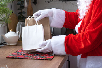 Santa Claus puts it on kitchen table and takes away paper bags with craft gift, homemade cakes and food delivery. Shopping, packaging recycling, handmade, delivery for Christmas and New year