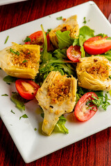 Grilled artichokes. Artichokes roasted in olive oil, topped with cheese sauce, garnished with scallions, parsley served in cast iron skillet. Classic American or French bistro side dish.