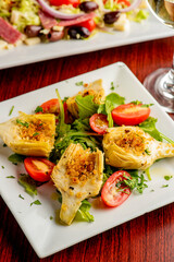 Grilled artichokes. Artichokes roasted in olive oil, topped with cheese sauce, garnished with scallions, parsley served in cast iron skillet. Classic American or French bistro side dish.