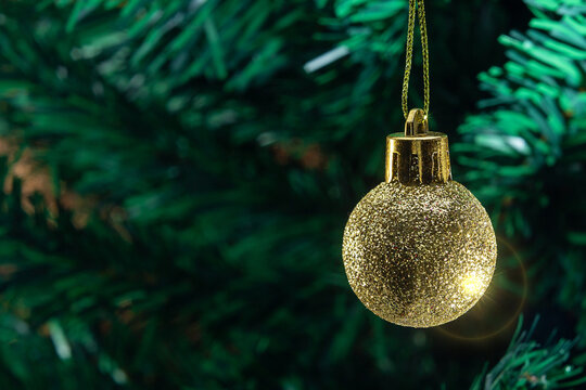 Uma bola dourada, pendurada no galho com detalhes da &aacute;rvore de natal ao fundo.