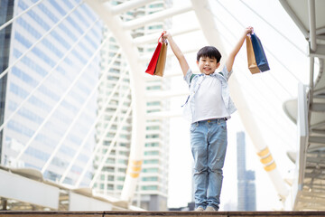 Cheerful happy Asian little boy carrying a paper shopping bags and smiling to camera.