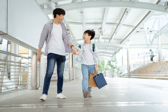 Father Taking His Son Going To School And Shopping, A Man Holding Child Hand While Walking Together In Downtown District.