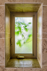 Small glass window of bathroom background with tiled shower interior of home house and green aspen foliage leaves on tree vertical view