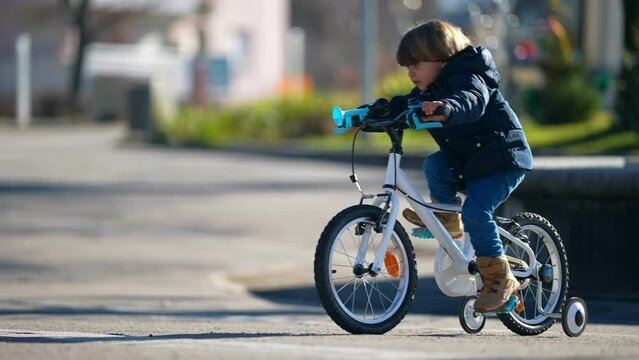 Child riding bicycle during winter season outside at city park. Kid cyclist learning to ride bike