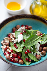 Salad with spinach leaves, pomegranate seeds, goat cheese and hazelnuts served in a turquoise bowl, vertical shot, close-up