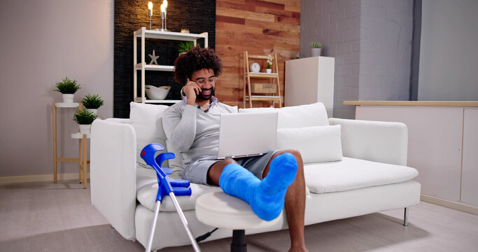 Happy Young Man With Broken Leg Sitting On Sofa Talking