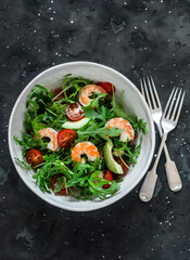 Salad with shrimp, arugula,avocado, cherry tomatoes on a dark background, top view