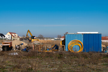 Obraz na płótnie Canvas Construction site with blue containers yellow coils of cable and excavator in the background. Clear blue sky.