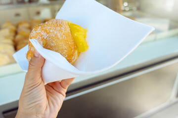 Hand holding Bola de Berlim or Berlim Ball, a Portuguese pastry made from a fried donut filled with sweet eggy cream and rolled in crunchy sugar.