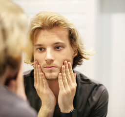 young man looking in the mirror,combing his hair,looking at problems on face.