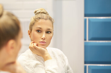 woman looking in the mirror in the bathroom and taking care of her skin.