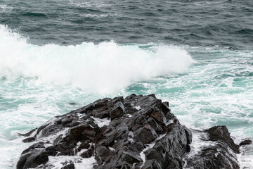 A seascape of a cloudy grey sky with a pink horizon that meets the grey ocean. There are a few...