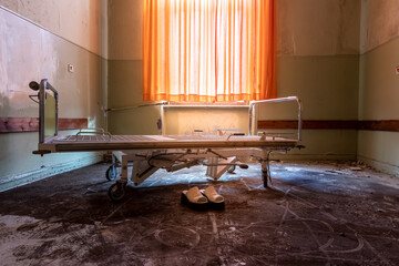 A very creepy and rotten hospital bed with ladies shoes in front of it.