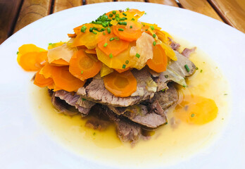 Classic Austrian Tafelspitz served with colorful root vegetables and broth, garnished with fresh chopped chives. A traditional boiled beef dish, typical of Viennese cuisine.