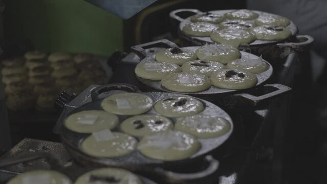 Video footage of a hand pouring cheese and meses topping into the Mud Cake or Kue Lumpur dough