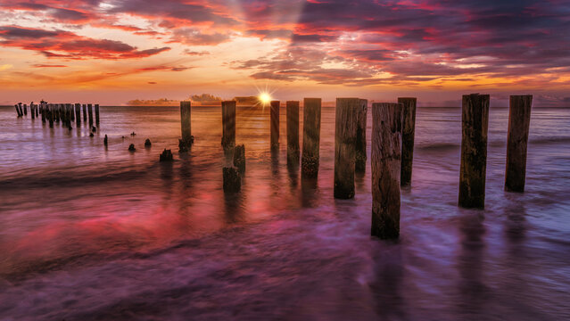 Abandoned jetty with nice sunset sky background and clear reflection from wet sand. Focus on the jetty piers. Travel and natural wonder.
