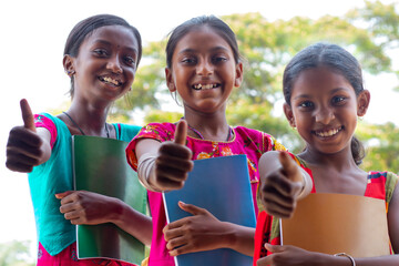 Smiling School girls showing thumbs up and holding books