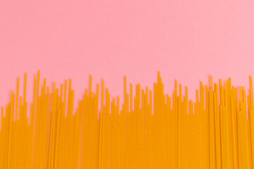 Raw macaroni scattered on pink background