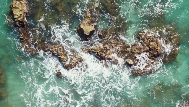 4K aerial shot from a drone, the purest turquoise waters break on the stone shore and rocks and foam. Surf splashes are scattered in slow motion