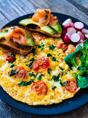 Breakfast - scrambled eggs with bacon and vegetables on black wooden table
