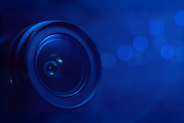Camera lens in smoke and blue light close-up, lights out of focus on the background