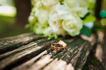 A pair of gold wedding rings on a brown background, in the background a bouquet with white flowers