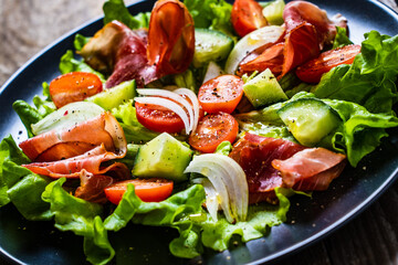 Tasty salad - prosciutto crudo and fresh vegetables on wooden table
