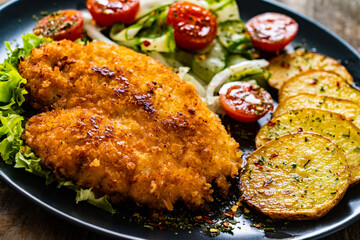 Breaded fried pork chop with fried potatoes and greens on wooden table

